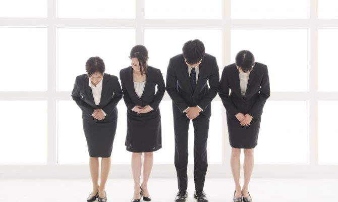 Four Japanese business people bowing at you
